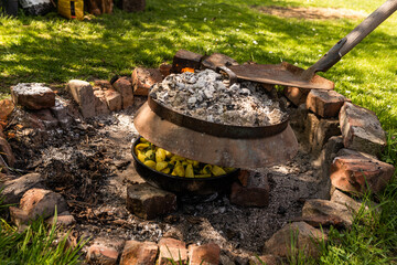 Cooking traditional dalmatian, croatian, bosnian dish called peka. Meat, potatoes and vegetables in pot and covered with hot charcoal and ash. Balkan food. - obrazy, fototapety, plakaty