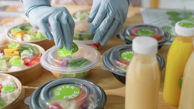 Close up shot hands of worker in gloves applying Eco Food sticker on container with salad while preparing orders at healthy meal delivery service