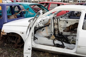 An old white wreck car with open door in a scrap yard that were cleared from interior