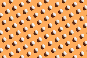 Minimal pattern made of white eggs under bright light with dark shadows on orange background