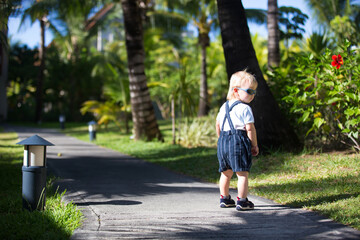 Fototapeta premium Adorable fashion baby toddler boy, dressed in casual clothes, walking in a beautiful resort gardens