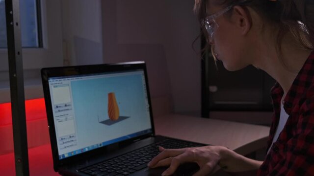Engineering female student using 3D printer. Creative STEM girl designer 3d printer to start it while sitting in front of laptop