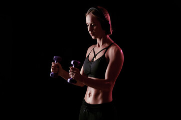 Young strong woman with perfect abdomen and strong arms exercise with dumbbells on black background