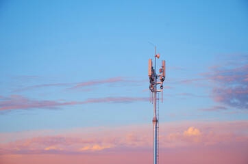 Cell tower on the background of the sunset sky with clouds