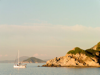 paesaggio marino con barca a vela e scogli al tramonto
