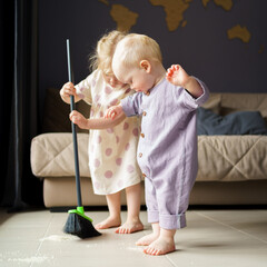 Cute little children infant boy and toddler girl in linen clothes sweeping floor in room with...