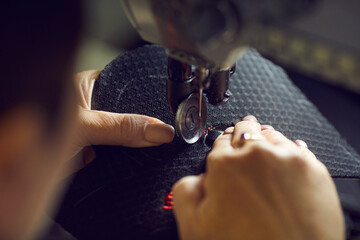 Female shoe factory worker using industrial sewing machine to make detail for new modern black sneakers, needle and hands holding shoe detail in closeup. Footwear manufacturing industry concept - Powered by Adobe