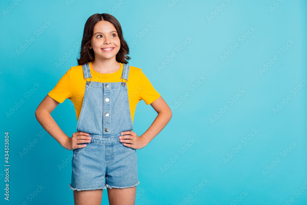 Sticker Photo of funny adorable small schoolgirl dressed yellow t-shirt arms waist looking empty space isolated blue color background