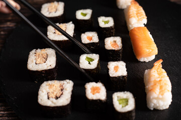 Sushi sind aufgelegt auf der schwarzen Platte, Schwarze Stäbe fassen ein Sushi an. Sehr gut geeignet für chinesischen Restaurant, Querformat.