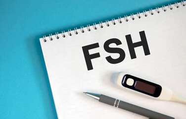 FSH text on a white notebook on a blue background with a pen and a medical thermometer