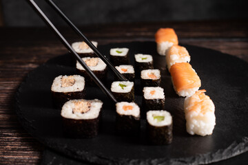 Verschiedene Sushi liegen auf dem schwarzen Brett. Die schwarze chinesische Stäbchen halten eine...