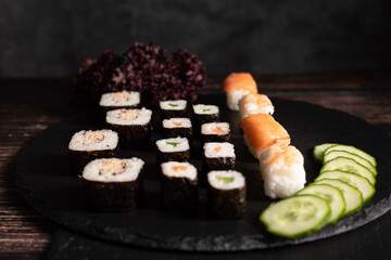 Sushi sind aufgelegt auf der schwarzen Platte, in Scheiben geschnittene Gurken und Salat im...