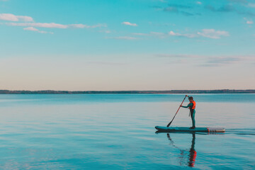 Kid riding on paddle sup surfboard in water at sunset