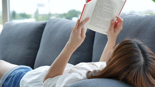 Relax asian woman reading book sitting on sofa in living room holding book to read. Young woman relaxation reader reading open book leisure mind. Happiness beauty woman person smiling face happy time