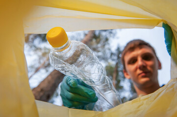 Garbage collection in nature. Young man puts plastic trash in a yellow bag, inside view