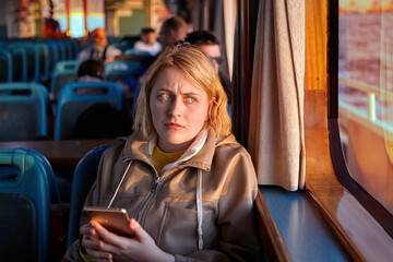 Fototapeta na wymiar Passenger cabin of ferry, offended young woman sits by window with smartphone in her hands.