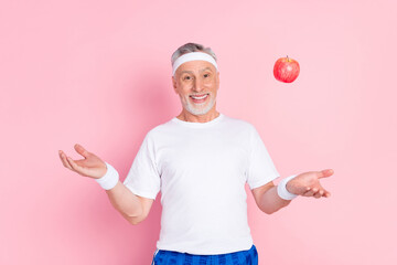 Photo portrait of senior man in headband keeping diet throwing apple isolated pastel pink color background