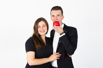 Young couple in black clothes eating red apple on a white background. The temptation and sin of Adam and Eve. young treats the viewer of apple