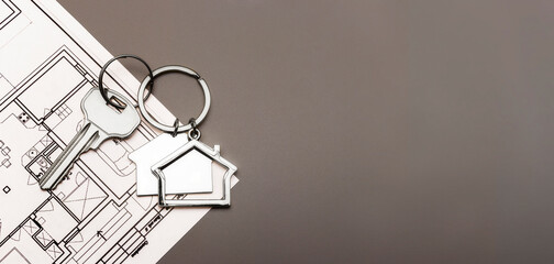The concept of mortgage and rental housing and real estate. Mortgage credit lending. Metal keychain in the shape of a house with a key on the plan of the house. Buying a house. Banner format.