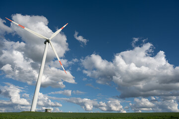 Windrad in grüner Landschaft vor blauem Himmel mit strahlend weißen Wolken