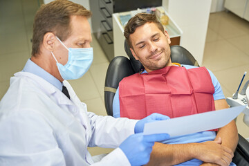 Fototapeta premium Contented patient and doctor looking at paper at dental clinic