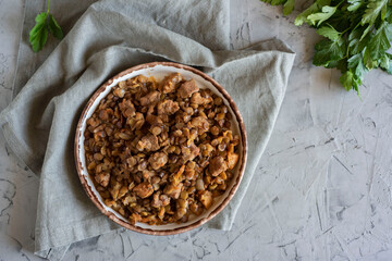 Lentils with meat and vegetables baked on a beautiful white plate on a gray background. Top view