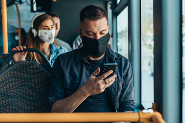 Man wearing protective mask and using a smartphone while riding a bus