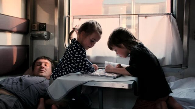 Boy and girl play while father lies on train sleeper shelf