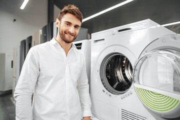 Obraz premium Young man choosing new washing machine in household appliances store