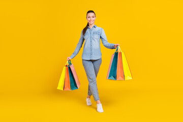Full body photo of cheerful lovely young woman hold hands bags shopping smile isolated on yellow...