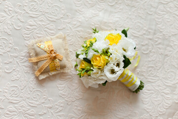 Tender Bride's bouquet in yellow and white colors and wedding rings on a pillow