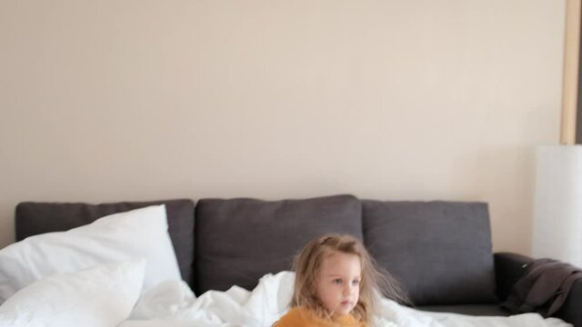 Small naughty girl jumps on sofa in spacious apartment room