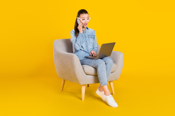 Full length body size woman sitting in chair talking on cellphone using laptop isolated bright yellow color background