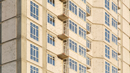 Fototapeta na wymiar Details of house under construction. Windows and balconies. Construction of multi-storey residential building. Crane build multi-storey residential house. Modern residential construction.