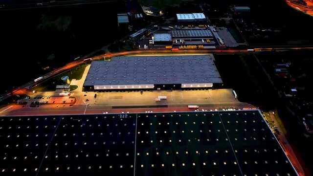 Aerial view of the large logistics park with warehouse, loading hub with many semi-trailers trucks standing at the ramps for load/unload goods at night.