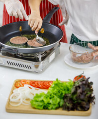 High angle of unrecognised people making patties on hot pan near woman in apron while cooking burgers in kitchen together.