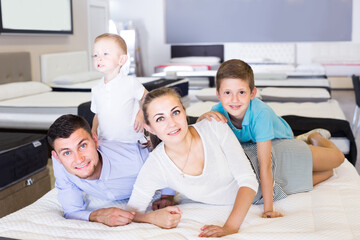 Smiling russian parents with two young sons testing mattress in store