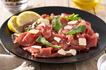 Marbled beef carpaccio on black plate on rustic wooden table