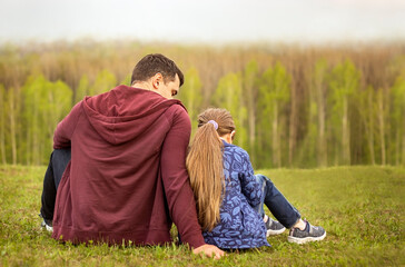 Dad and daughter sit with their backs outdoors in the forest. The concept of family relationships. Overcast