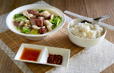 Boiled soup blood pork in bowl and flavouring in white bowl on bamboo mat,
