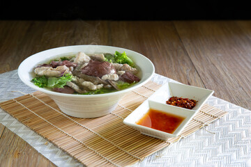 Boiled soup blood pork in bowl and flavouring in white bowl on bamboo mat