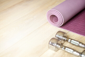 rolled yoga mat and metal dumbbells lie on the wooden floor in the sunlight. Soft focus in the light of the sun