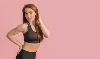 Fototapeta na wymiar Fitness girl smiling in black sportswear on a pink background. Slim woman with a beautiful athletic body and tanned skin