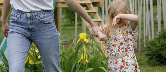 Mother pulling stubborn toddler girl in public park. Girl does not want to leave a playground. Problem of leaving the playground.
