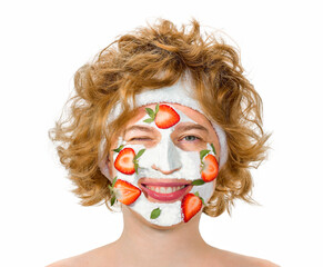 Red-haired curly young woman with a positive cheerful mood, smiling and winks, closed eye. With a cosmetic mask on the face of strawberries and cream.