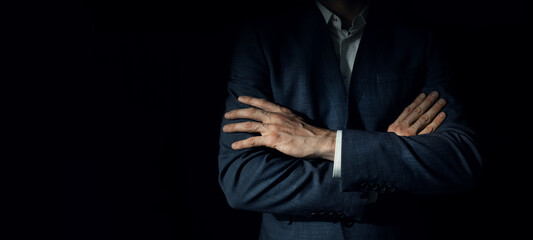 businessman in suit with crossed arms standing on dark black background. copy space - Powered by Adobe
