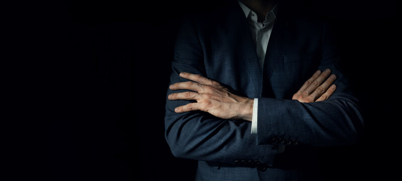 businessman in suit with crossed arms standing on dark black background. copy space