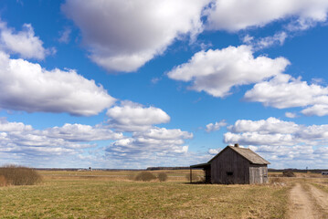 An old abandoned small wooden house in the fields sky clouds, barn or scary concept.