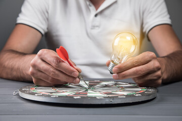 a man puts a dart in the center of a dart board and holds a light bulb. concept ideas and goals