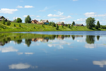 Fototapeta na wymiar Idyllic rural landscape. Small village by the lake on a sunny summer day. The clouds are reflected in the lake